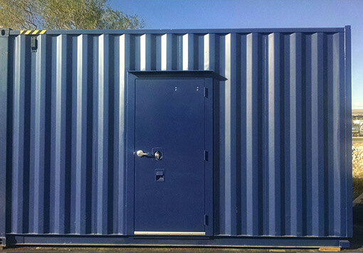 a blue storage container with a blue door, behind the container is a tree and the blue sky.