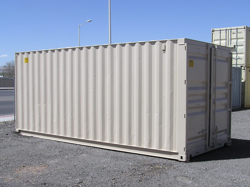 A 20ft storage container with a dirty white painted on it, behind the container are more storage containers and a road.