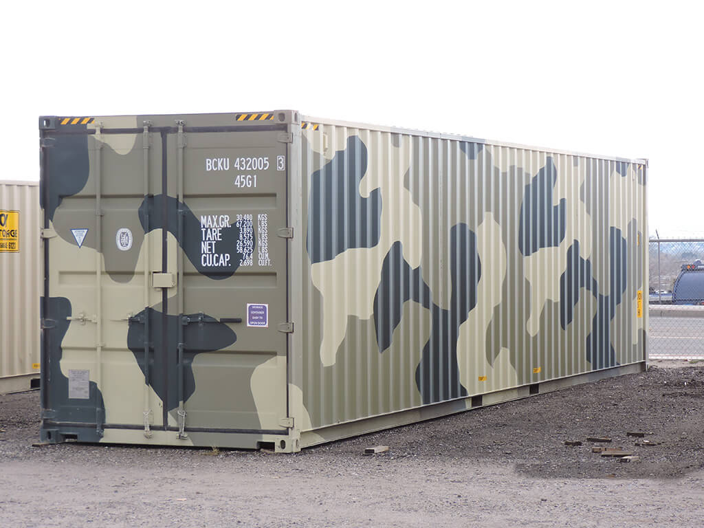 a storage container that was painted in Camouflage, it is a 40ft storage container, beside it is another storage container colored in dirty white.